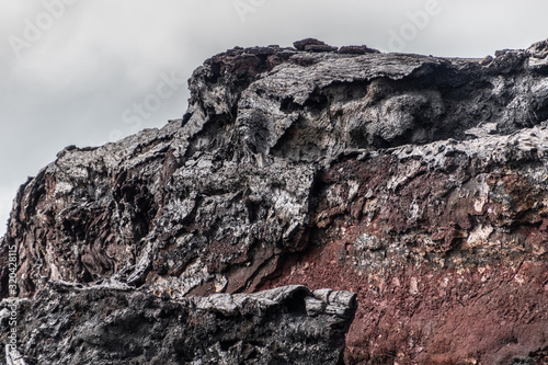 Leilani Estate, Hawaii, USA. - January 14, 2020: 2018 Kilauea volcano eruption hardened black lava field. Closeup of cliff that lost its shell exposing red rock under. Gray sky. photo