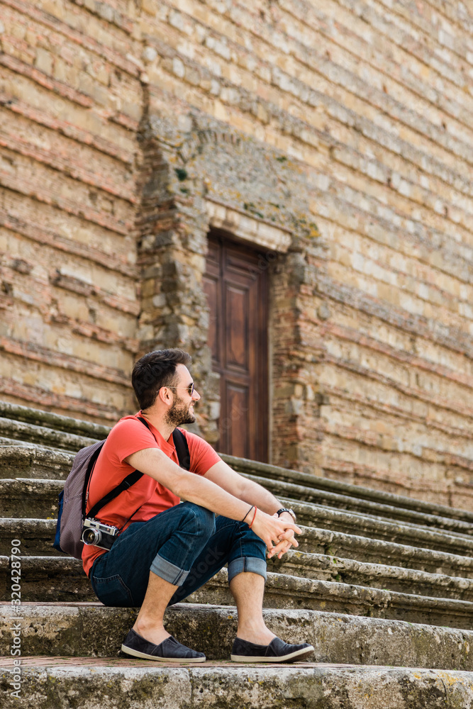 Young male traveler sitting on steps in old town in Tuscany, Italy