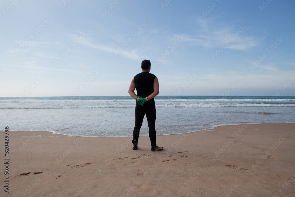 Swimmer in wetsuit on beach looking out over ocean Swimmer in wetsuit on beach looking out over ocean