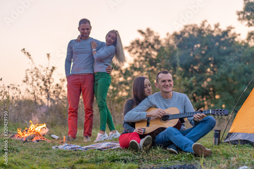 Group of happy friends with guitar, having fun outdoor, near bonfire and tourist tent. Camping fun happy family © Kate