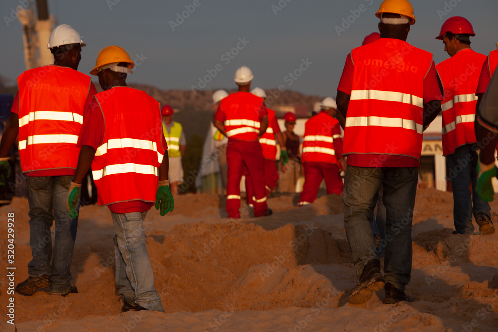 Workers in reflective clothing on sandy beach against sky Workers in reflective clothing on sandy beach against sky