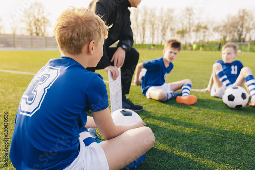 Young Soccer Trainer Coach Explaining Tactic on Team Sports Tactics Board. Children During Soccer Football Coaching Session. Boys in Soccer Team Listening to Coach