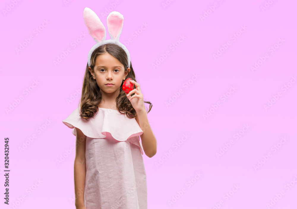 Brunette hispanic girl wearing easter rabbit ears with a confident expression on smart face thinking serious Brunette hispanic girl wearing easter rabbit ears with a confident expression on smart face thinking serious