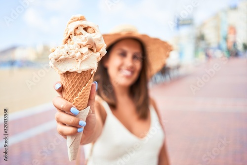 Fotografia, Obraz Young beautiful woman eating ice cream cone by the beach on a sunny day of summe