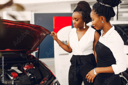 Women buying the car. Ladies in a car salon. Black girls near red car