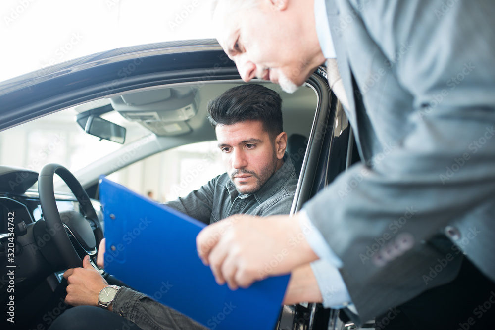 Young smiling man taking taking look to car in showroom Young smiling man taking taking look to car in showroom