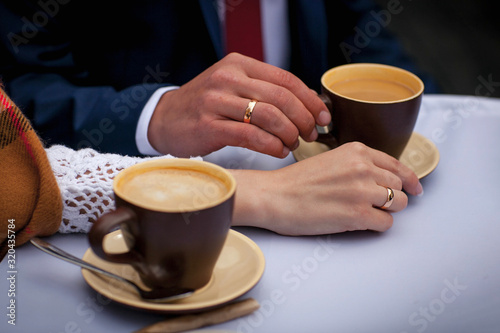 Two hands, male and female, with the wedding rings touch of brown coffee cup