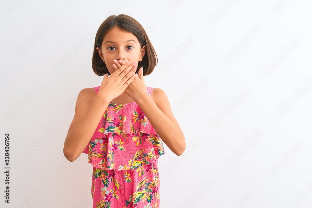 Young beautiful child girl wearing pink floral dress standing over isolated white background shocked covering mouth with hands for mistake. Secret concept. Young beautiful child girl wearing pink floral dress standing over isolated white background shocked covering mouth with hands for mistake. Secret concept.