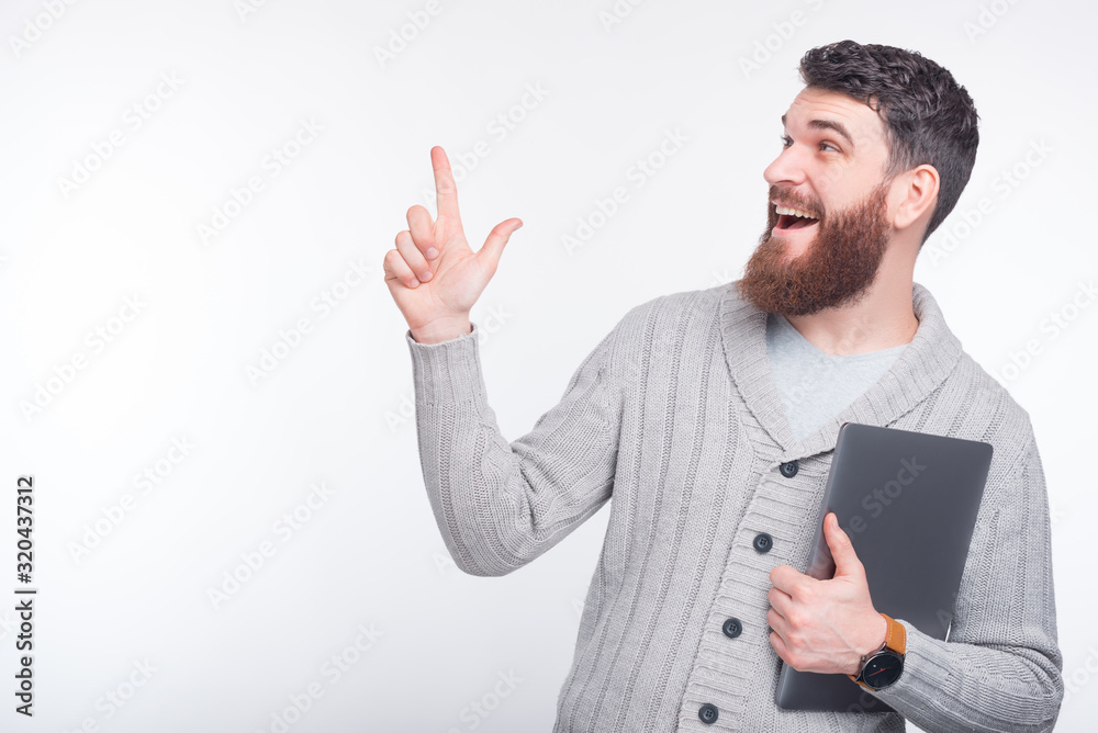 Man is pointing upwards on white background and holding his laptop. Man is pointing upwards on white background and holding his laptop.