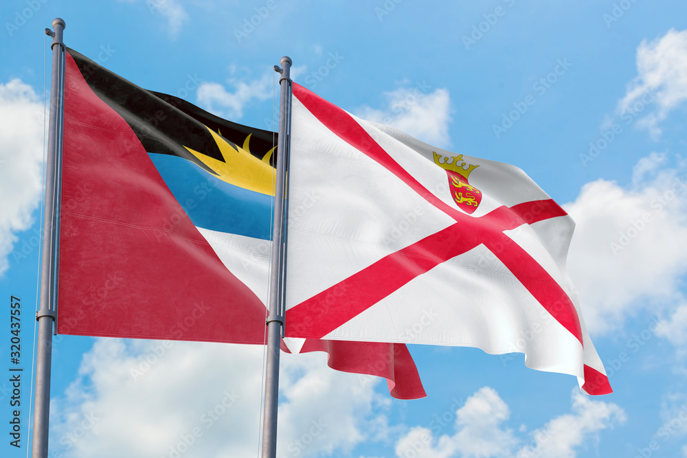 Jersey and Antigua and Barbuda flags waving in the wind against white cloudy blue sky together. Diplomacy concept, international relations.