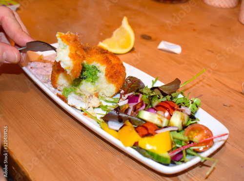 Man eating with fork homemade minted mushy pea fishcake containing cod salmon smoked haddock Seafood starter garnished with fresh vegetable salad including cherry tomatoes peppers spring onion lettuce photo