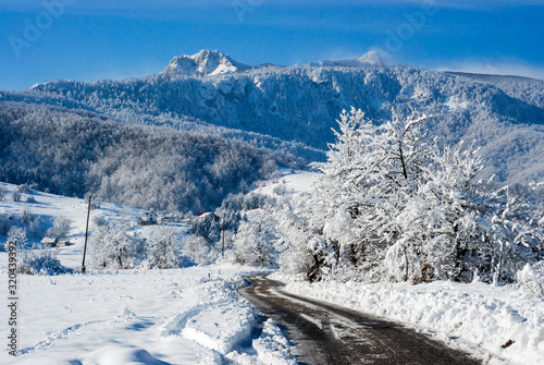 Winter road in snowy forest. Winter scene in mountains. Forest and hills covered with a snow. Snowy trees after heavy snowfall. Cold winter day in nature. Beautiful Landscape. Wilderness. 