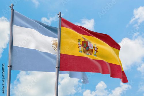 Spain and Argentina flags waving in the wind against white cloudy blue sky together. Diplomacy concept, international relations.