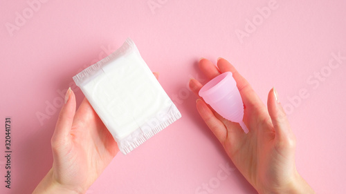 Female hands holding sanitary pad and menstrual cup over pink background. Different types of menstrual hygiene products comparison. Critical days, menstruation cycle, female healthcare concept photo