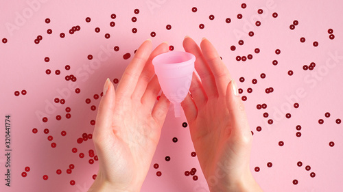 Woman hands holding menstrual cup over pink background with confetti. Eco-friendly menstrual hygiene product. Critical days, menstruation cycle, female healthcare concept photo