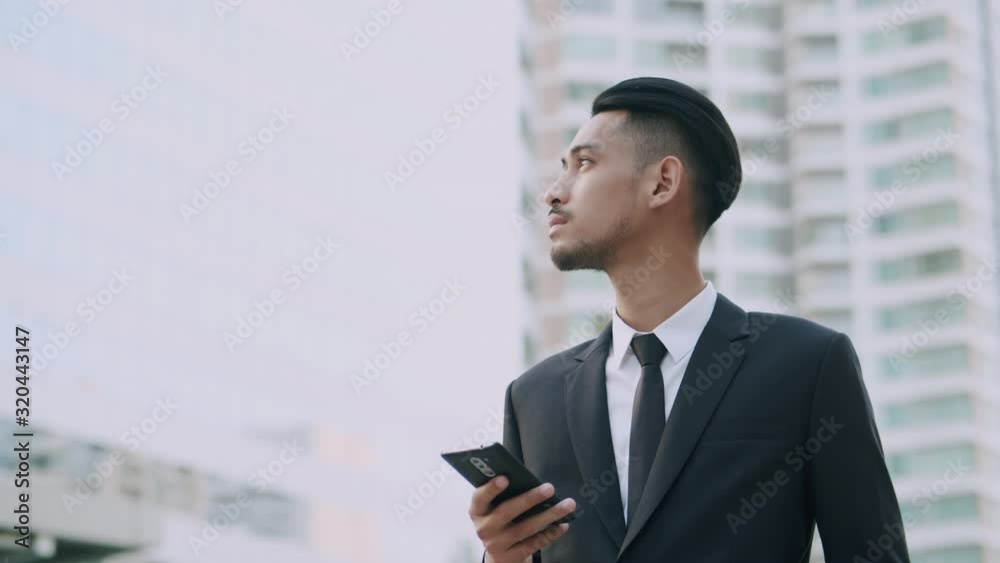 Medium shot of Young asian businessman while stand using smart phone in the city, Business, technology and people concept, Camera rotating around his Medium shot of Young asian businessman while stand using smart phone in the city, Business, technology and people concept, Camera rotating around his