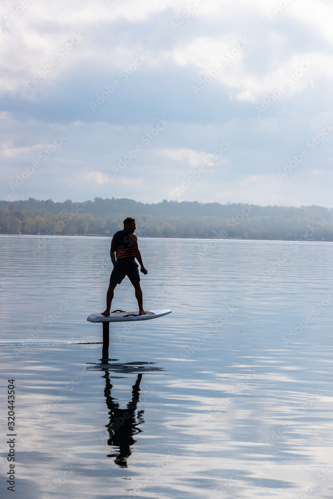 Man riding an electric hydrofoil foil board on a lake with a life jacket