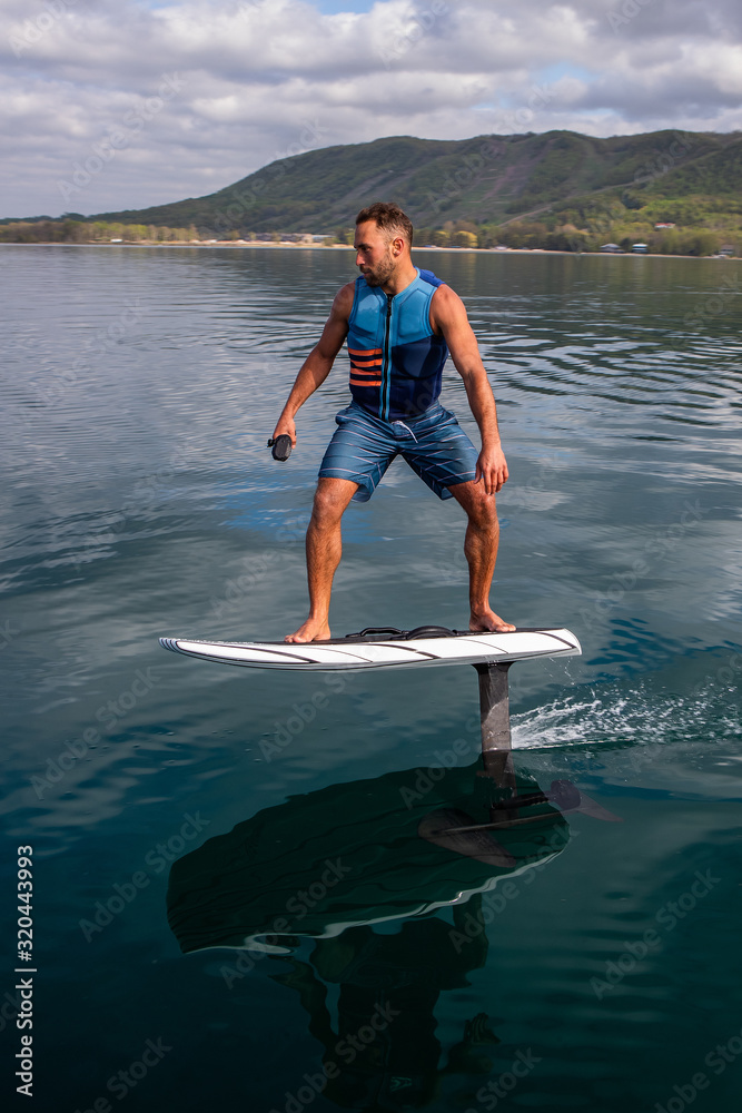 Man riding an electric hydrofoil foil board on a lake with a life jacket