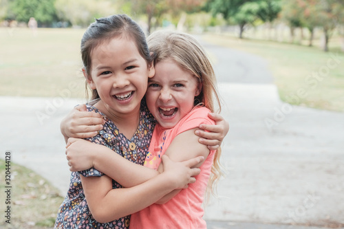 Obraz na płótnie Happy and healthy mixed race multiethnic young little girls hugging and smiling in the park, best friend kids and children friendship concept