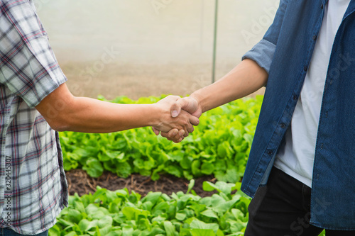 Handshake of business partners, farmers on green farm background. Farmer with tablet for working organic hydroponic vegetable garden at greenhouse.
