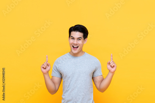 Happy smiling young Asian man with hands poiting up
