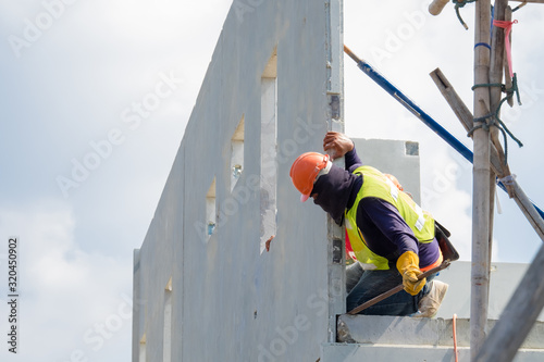 Construction worker are installing the precast concrete wall, orange safety helmet and green vest.
