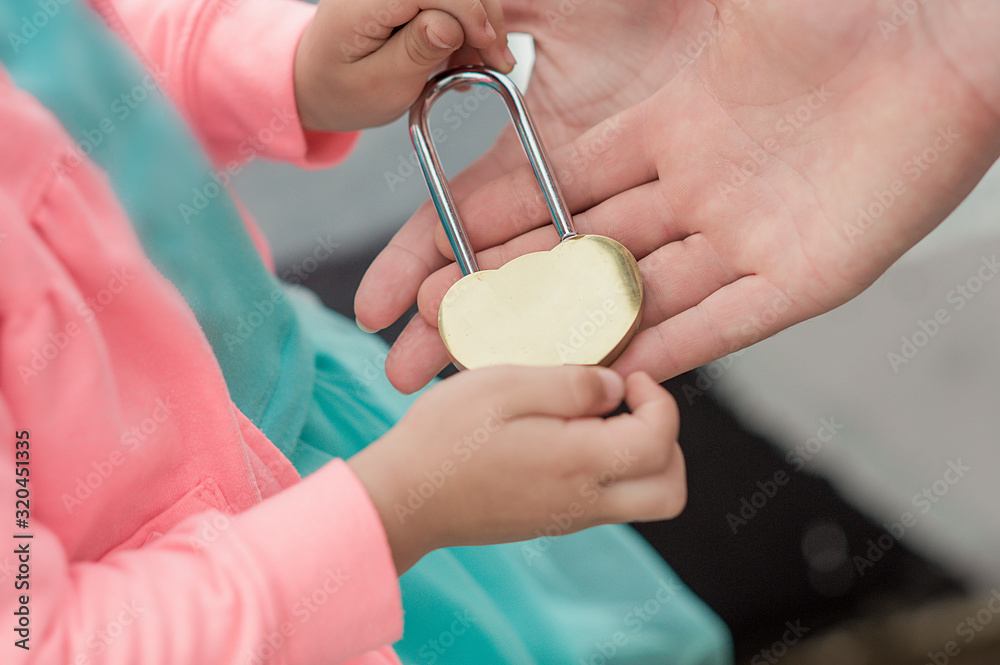 Fototapeta premium unusual metal gold closed lock in hands, a little girl passes the lock to a large adult hand