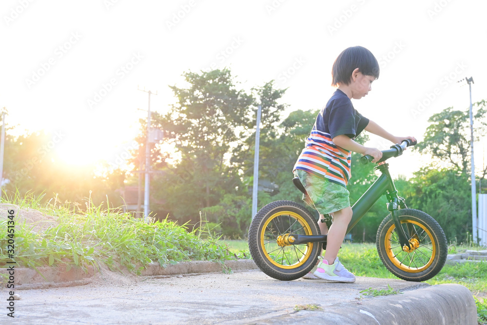 cute boy playing balance bike in the park with sun light in the morning day