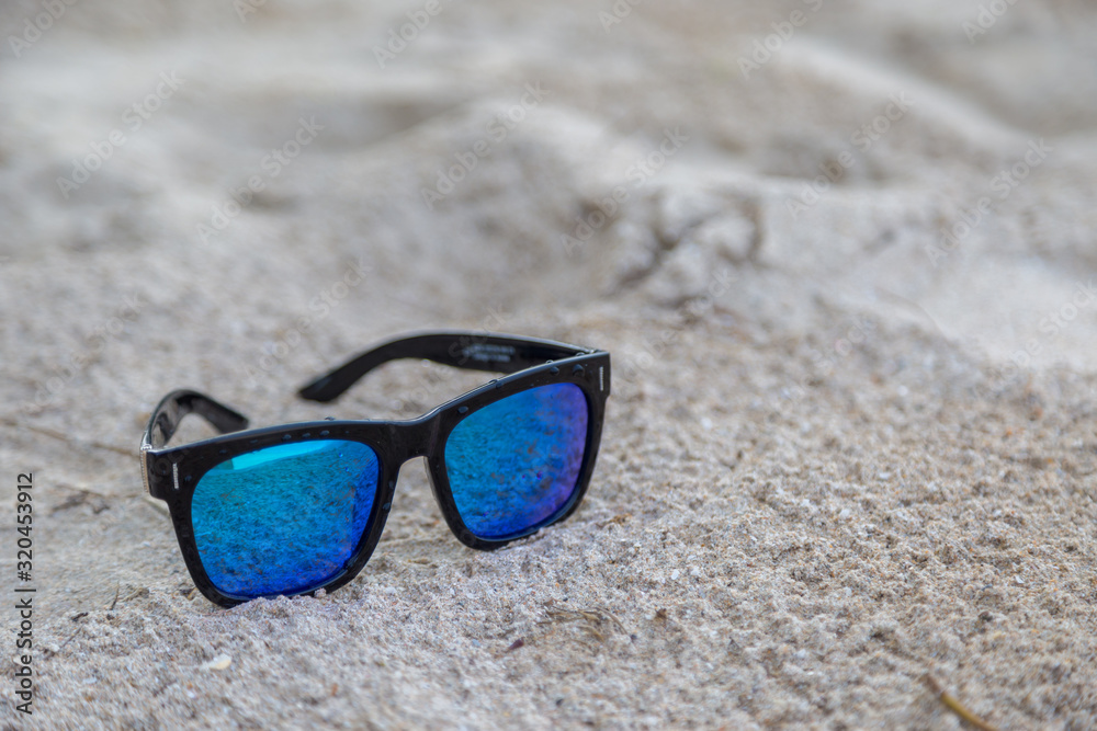 Blue sunglasses on white sand