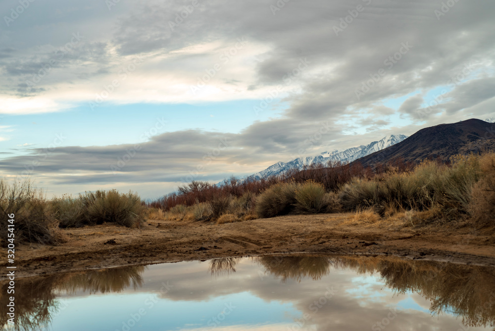 California valley view with snowy Sierra Nevada mountain range reflected in rain puddle in dirt road