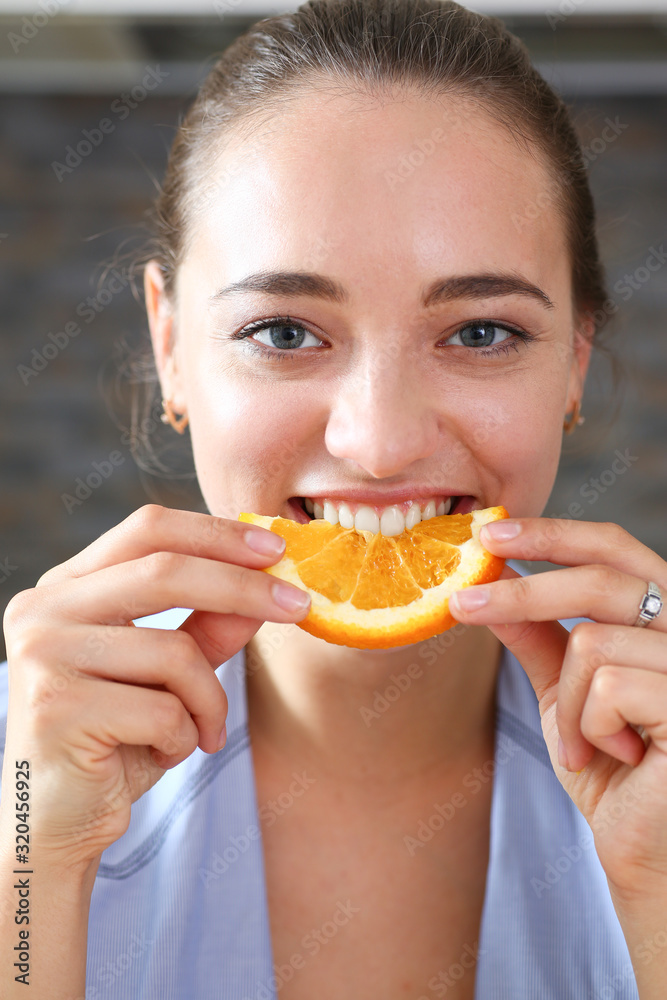 Woman portrait holds in her hand a slice of chopped orange eats her for breakfast with her mouth in the kitchen concept of a healthy diet.