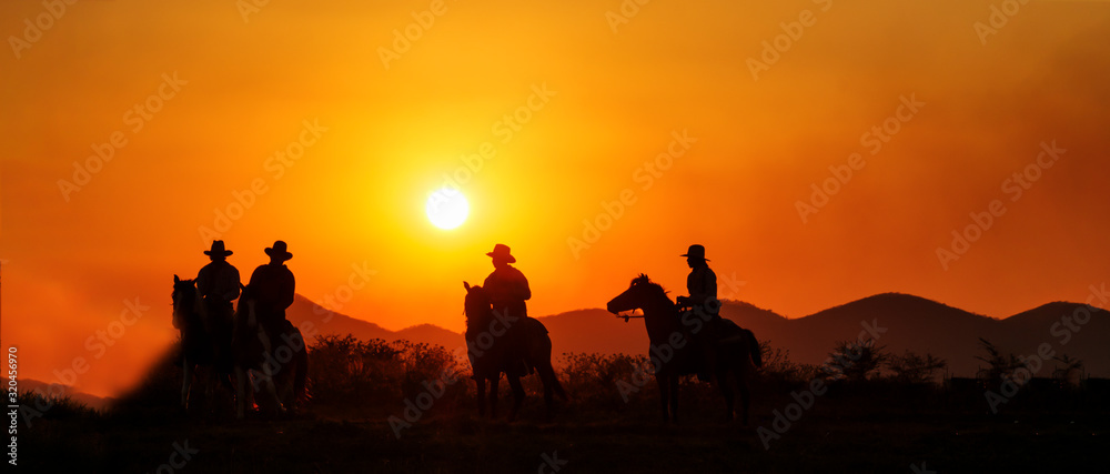 Silhouette cowboy group riding horseback at sunset, panoramic landscape