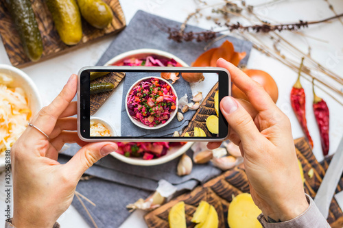 Take phone picture of healthy vegan food at kitchen on table. Smartphone food photography of vinaigrette russian salad with pickled vegetables photo