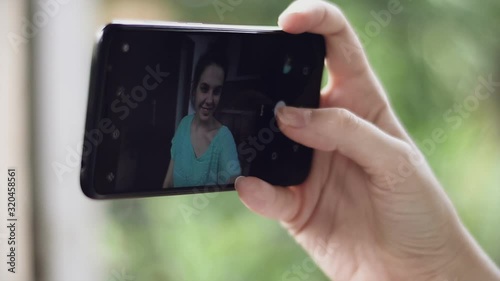 Young pretty woman takes selfie. Closeup hand holding phone.