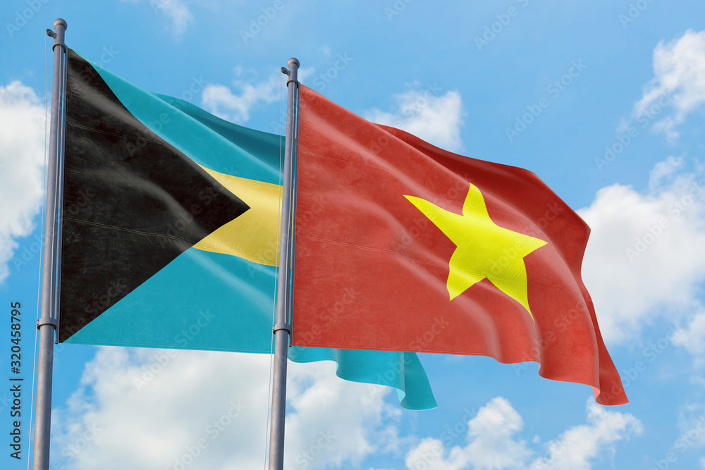 Vietnam and Bahamas flags waving in the wind against white cloudy blue sky together. Diplomacy concept, international relations. Vietnam and Bahamas flags waving in the wind against white cloudy blue sky together. Diplomacy concept, international relations.