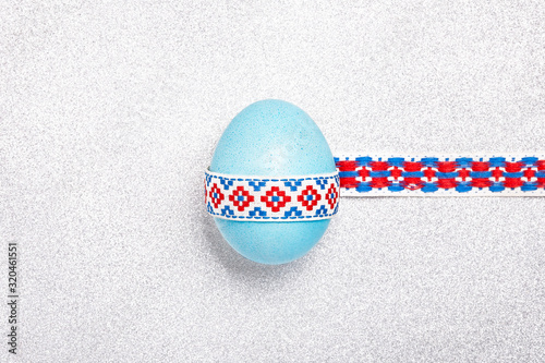 Blue shine egg with a national traditional ribbon on a silver glitter background