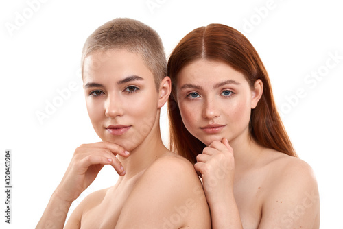 Extremely close. Beauty portrait of two young different women with clean and fresh skin looking at camera and smiling while posing naked against white background. Blonde and red hair models