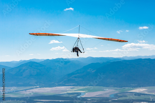 Hang glider man flying in clear sunny day. Flight over Kootenay valley mountains, Creston, British Columbia, Canada. Long shot photo