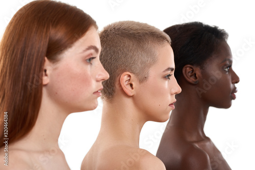 Different skin tones. Side view of three beautiful multicultural young women.Two caucasian and african half naked women posing in studio over white background. Natural beauty