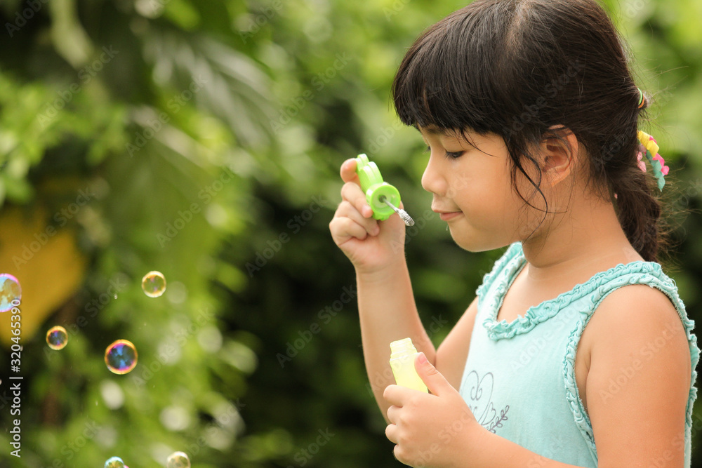 A little girl blowing soap bubbles in garden 