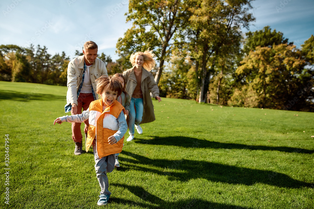 Fototapeta premium Catch me. Excited family running outdoors on a sunny day