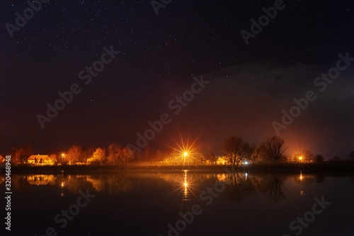 A magical starry night on the river bank with a large tree and a milky way in the sky and falling stars