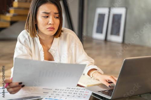 Sad Asian young woman working with papers and laptop