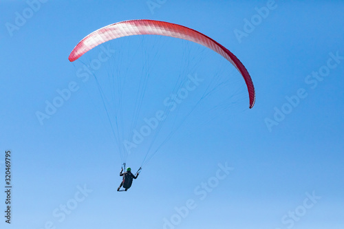 Beautiful flight of paraglider against the blue sky. Long shot of flying paraglider man. Recreational and competitive adventure sport