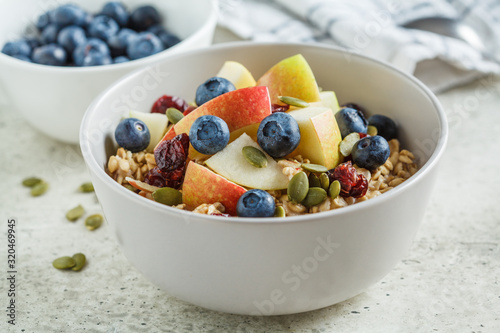 Bircher muesli or overnight oatmeal with apple, banana and blueberries in gray bowl.