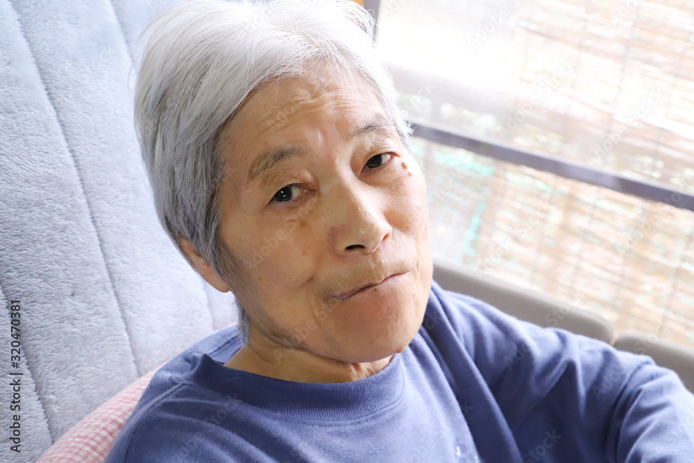 介護用ベッドに座ってこちらを見ながらはにかんだ顔をするシニア女性 介護用ベッドに座ってこちらを見ながらはにかんだ顔をするシニア女性