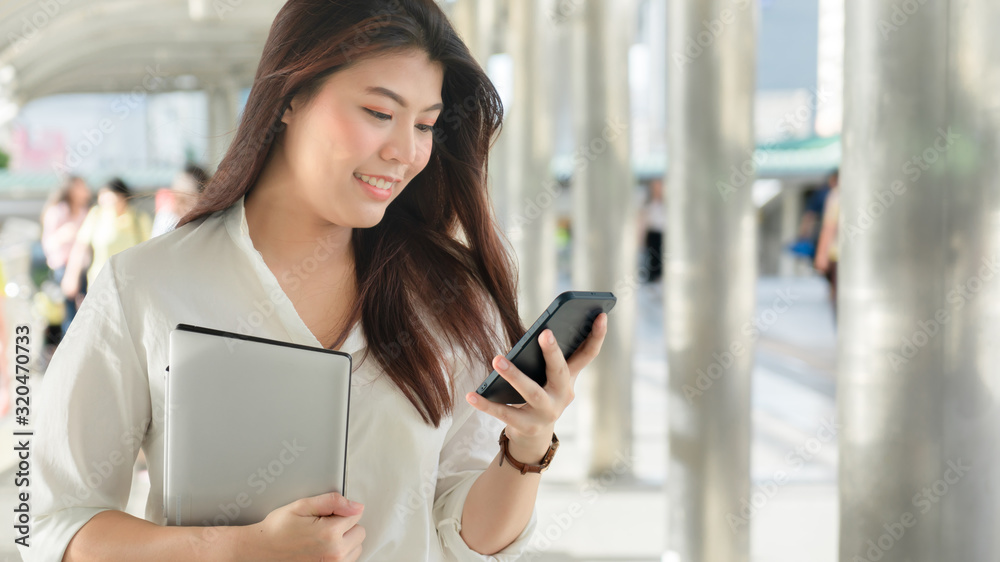 Business woman smiling holding laptop use smartphone working to outdoor city.