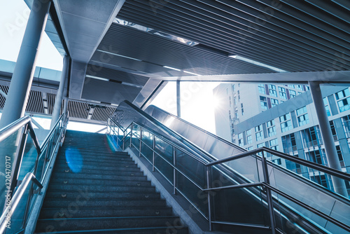 Outdoor elevators and city buildings, with sunlight in front.