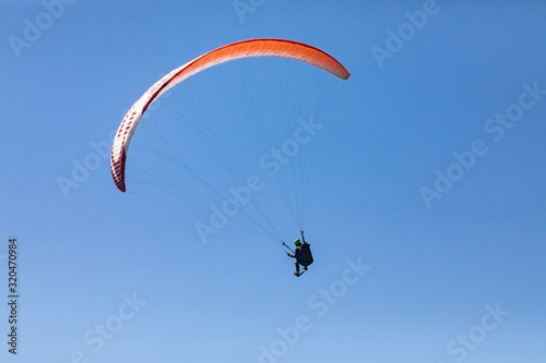 Long shot of flying paraglider against the blue sky. A bright red paraglider flies in the sky. Practicing extremal air sportsman