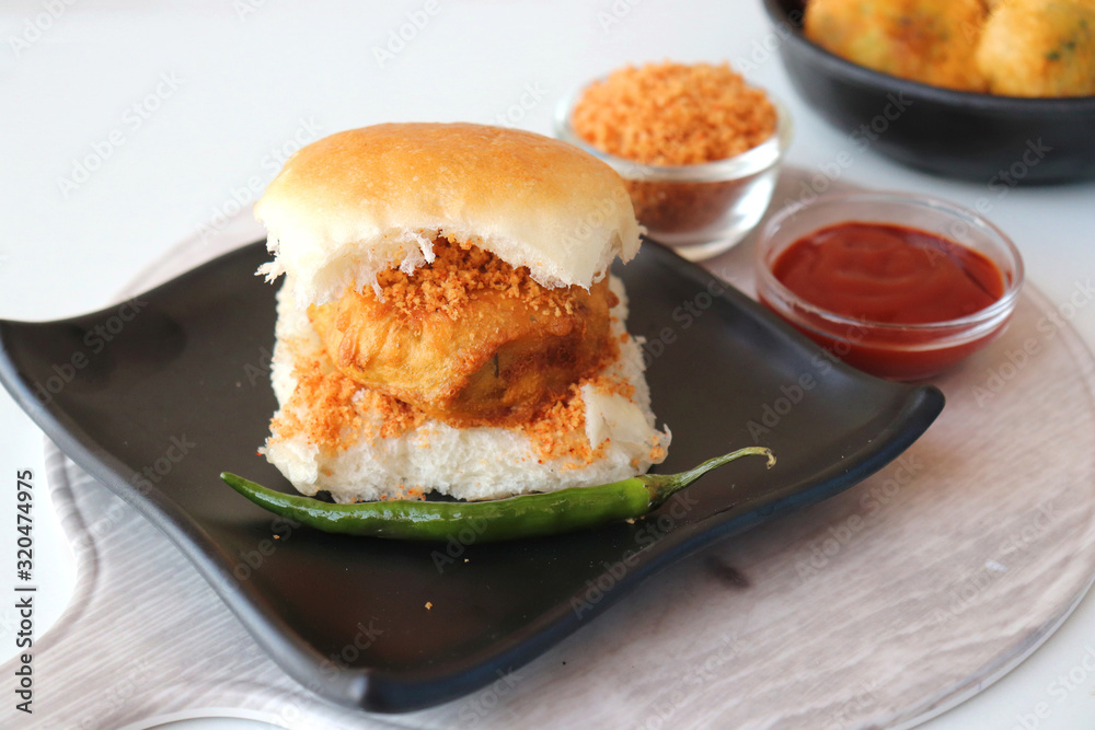 Vada pav or wada pao is a vegetarian fast food dish native to the state of Maharashtra. Famous Mumbai street food served with Red chutney and fried green chili. Copy space Vada pav or wada pao is a vegetarian fast food dish native to the state of Maharashtra. Famous Mumbai street food served with Red chutney and fried green chili. Copy space